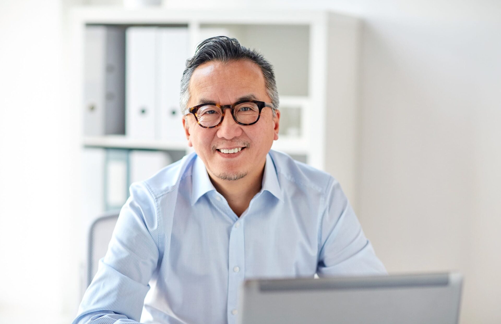 business, people and technology concept - happy smiling businessman in eyeglasses with laptop computer office